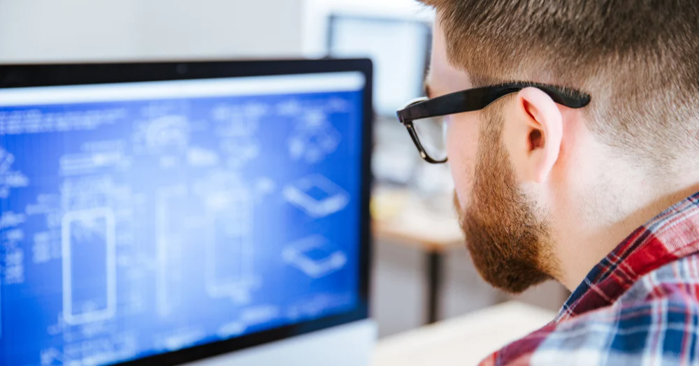 Closeup of young man in glasses with beard making blueprints on computer