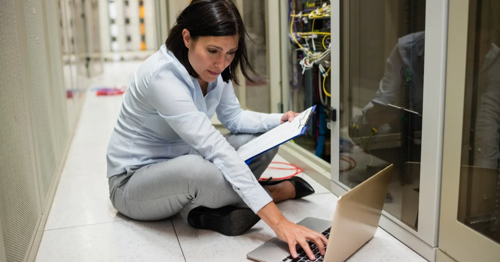 Technician checking clipboard while working on laptop